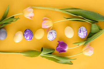 Obraz na płótnie Canvas Easter yellow background with pink and purple tulips and Easter eggs