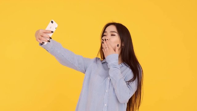 Asian Girl on yellow background makes a selfie and sends pictures over Internet
