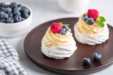 Delicious Pavlova cake with whipped cream and fresh berries on wooden plate. Selective focus