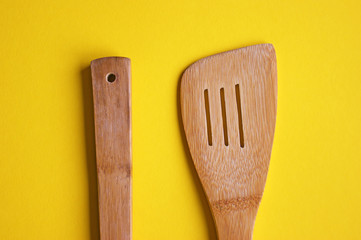 Top view of wooden kitchen spoon and spatula isolated on yellow background.