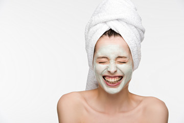 excited girl with facial nourishing mask and towel on head laughing with closed eyes isolated on white