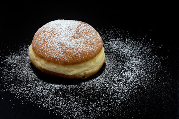 Einzelner Krapfen mit Puderzucker auf schwarzem Untergrund