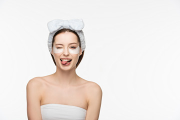 cheerful girl with eye patches winking and sticking out tongue while looking at camera isolated on...