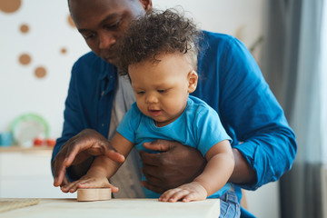 Portrait of cute African-American toddler playing with wooden toys together with dad, copy space