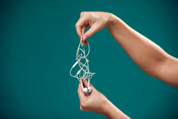 Woman holding tangled earphone trying to untangle it. People and technology concept