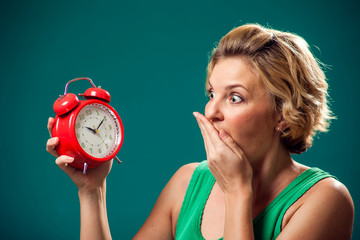 A portrait of surprised woman holding alarm clock. People and emotions concept