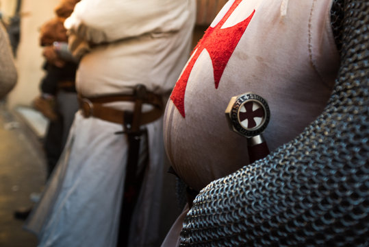 A close shot of persons torso dressed up historically to mimic a knights templar in full armor with his sword visible in the belt. Fat Templar, gut with the red cross.