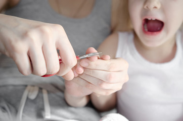 mother cuts her daughter's nails with scissors in the bedroom - focus on her hands. baby hygiene