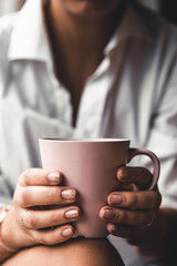 Woman in a white t-shirt holds morning coffee in a pink ceramic cup. Manicure. Front view