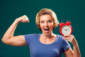 A portrait of smiling woman holding alarm clock and showing her bicep. People and emotions concept