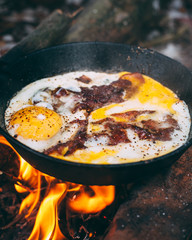Fried eggs with bacon in a pan in the forest. Food at the camp. Fried egg with bacon on fire. Picnic