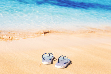 Striped marine flip flops on a sandy beach and clear blue sea ocean waters. Exotic vacation and...