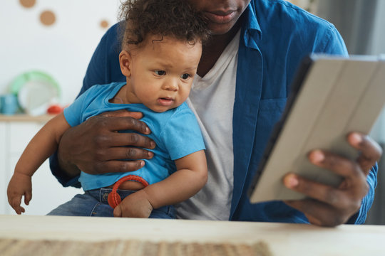 Cropped portrait of African-American man holding baby while using digital tablet in home interior, copy space