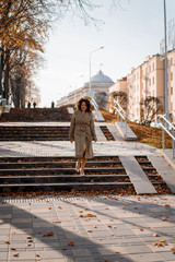 a young woman walks through the autumn city, a happy body female with curly hair in a raincoat.