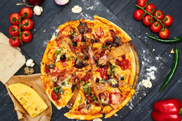 Pizza with mozzarella cheese, tomatoes, mushrooms, peppers, herbs on a dark wooden background.
