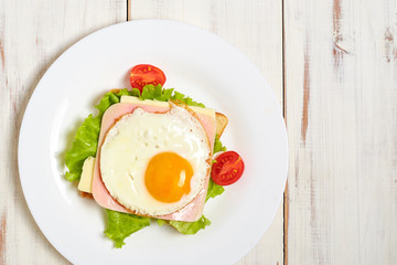 Toast with ham, egg and tomato on a plate on a light wooden background.