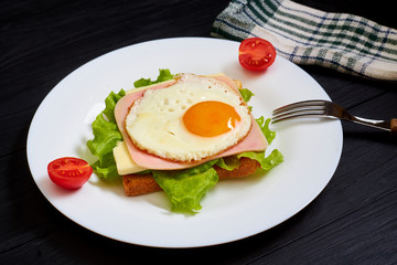 Toast with ham, egg and tomato on a plate on a black background.