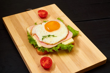 Toast with ham, egg and tomato on a light wooden board.