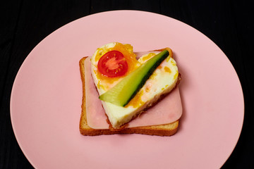 Toast with ham, heart-shaped egg and tomato on a pink plate.