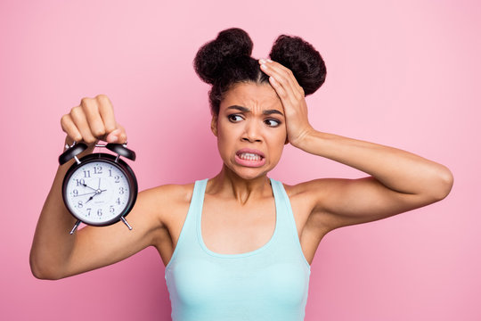 Photo of funny dark skin lady hold metal classic alarm clock hand on head grimacing oversleep missed work afraid to be late wear blue tank-top isolated bright pink background