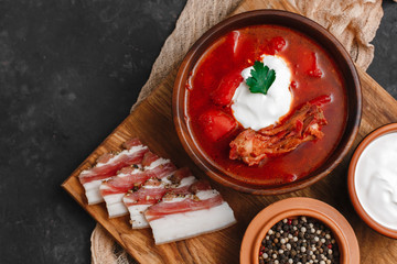 Ukrainian borsch. Beetroot soup. Ukrainian cuisine.In a wooden plate with salted bacon, bread and herbs. On dark background. The view from the top. Free space for your text. A bowl of red beet soup wi