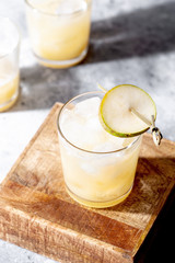 Cold pear cocktail or mocktail with soda and pear puree and fruit slices in short glass on gray background with shadow close-up. Refreshing summer drink with ice. Vertical orientation