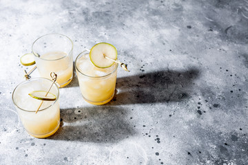Cold pear cocktail or mocktail with soda and pear puree and fruit slices in short glass on gray background with shadow. Refreshing summer drink with ice. Horizontal orientation, copy space