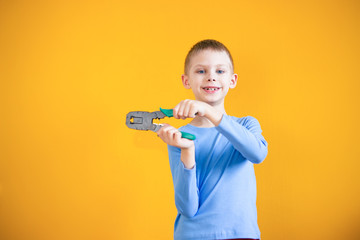 the child on an orange background holds in his hands a work tool, crimp for internet cable and smiles