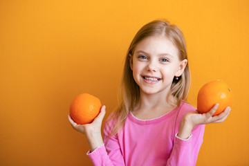 Cute baby 8 years old on an orange background, blonde pretty girl with appelsins in her hands smiles