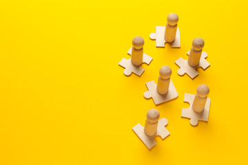Wooden figures on puzzles on yellow background as a symbol of team building. Organization group people in business. Cooperation and partnership.
