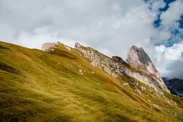 Incredible views of the peaks of Seceda in South Tyrol in the Alps of Italy. Partly cloudy around the mountains. Green slopes and blue sky. Travel and hiking