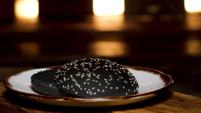 Close up of black bread with sesame seeds lying on a plate on the wooden table. Stock footage. Homemade bread for hamburgers preparation.