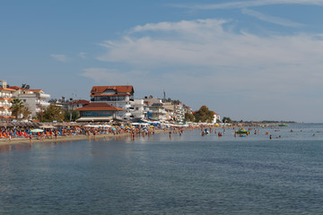 PARALIA, GREECE - SEPTEMBER 10, 2018: Beach scene. People swimming and sunbathing on the comfort shallow water coast full of budget hotels