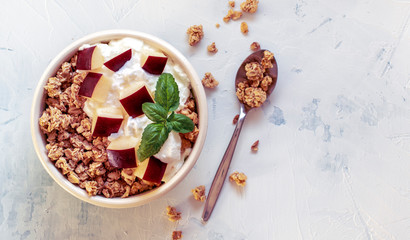 Bowl of granola with yogurt, cut apples and basil on textured white table. Healthy breakfast. Top view. Copy space for text.