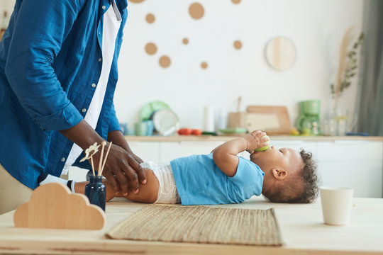 Side View At Unrecognizable Father Changing Diaper To Cute African-American Toddler Eating Apple, Copy Space