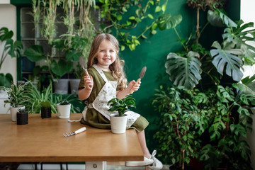 A little blonde girl in a greenhouse is gardening. Planting plants.