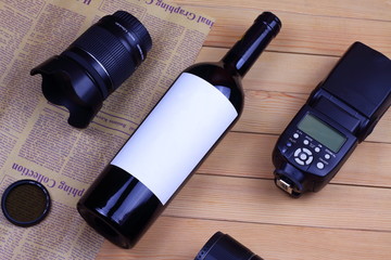 Red wine bottle with white paper, lens, speedlight and filter with vintage paper on background wooden table.