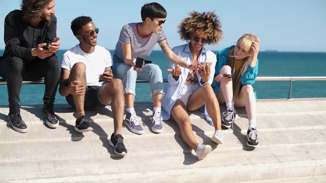 Contemporary diverse friends with smartphones on seafront