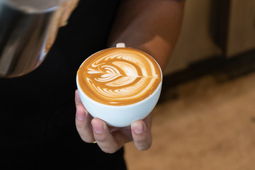 Latte art by barista focus in milk and coffee.Professional barista pouring steamed milk into coffee...