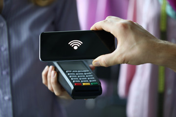 Man through terminal using Pay Pass technology. Phone with contactless payment technology allows you to pay for purchases much faster. Pay for shopping with mobile device, on phone an NFC chip