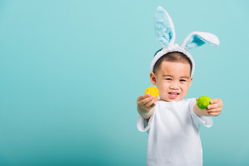 child boy wearing bunny ears and white T-shirt, standing to holds easter eggs