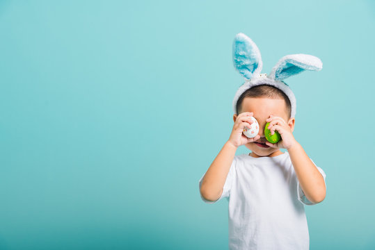 Child Boy Wearing Bunny Ears And White T-shirt, Standing To Holds Easter Eggs Instead Of Eyes