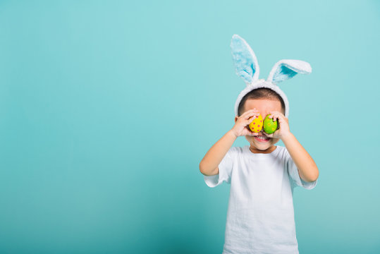 child boy wearing bunny ears and white T-shirt, standing to holds easter eggs instead of eyes