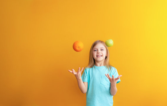 Cute baby 6-8 years old, baby girl blonde beauty on an orange background throws and catches fruit and laughs, apple and appelsyn