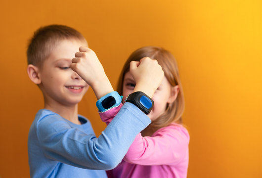 Happy children 6-8 years old with a smart GPS watch talking to parents safely. orange background