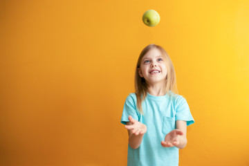 Cute baby on an orange background, 6-8 years old, baby girl throws an apple up