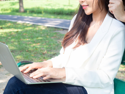 two asia business woman working with computer laptop in park. beauty woman tpying keyboard notebook blank screen and friend standing behind with copy space.  