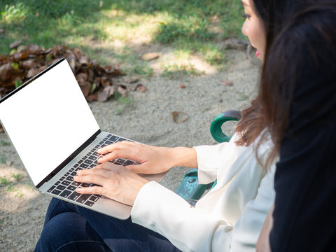 two asia business woman working with computer laptop in park. beauty woman tpying keyboard notebook blank screen and friend standing behind with copy space.  