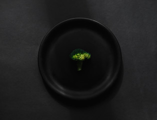 Broccoli in black plate on dark black background. Top view, flatlay and healthy diet concept.