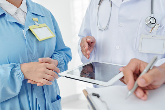 Cropped image of doctors reading list of symptoms on tablet computer and making diagnosis together